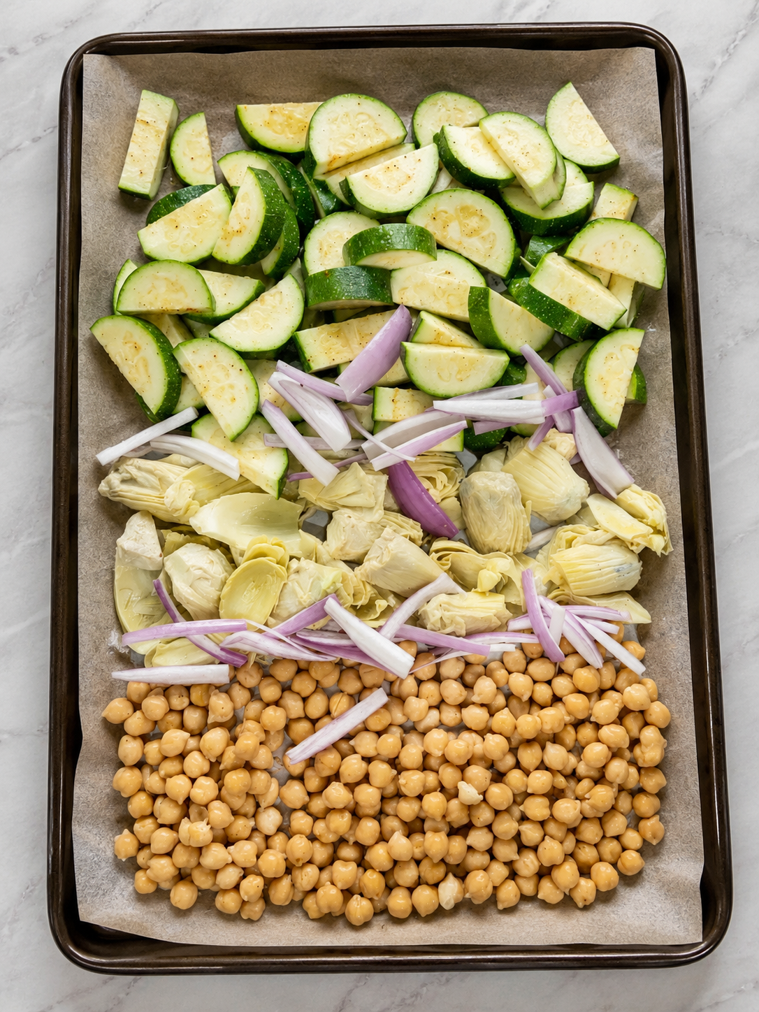 Sheet pan with zucchini, artichoke hearts, red onion, and chickpeas before roasting